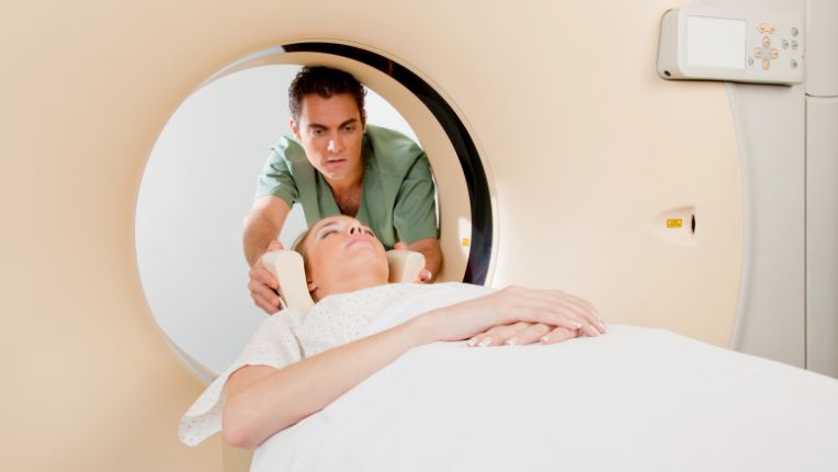 Quelle est la différence entre une radio et un scanner ? Patiente à l'entrée de l'anneau d'un scan, en train d'être installée par un soignant.