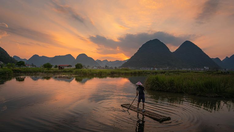Vaccin encéphalite japonaise CVI Lyon Parc Elsan. Vue d'un étang dans un pays asiatique montagneux sur lequel se déplace un homme sur une barge.