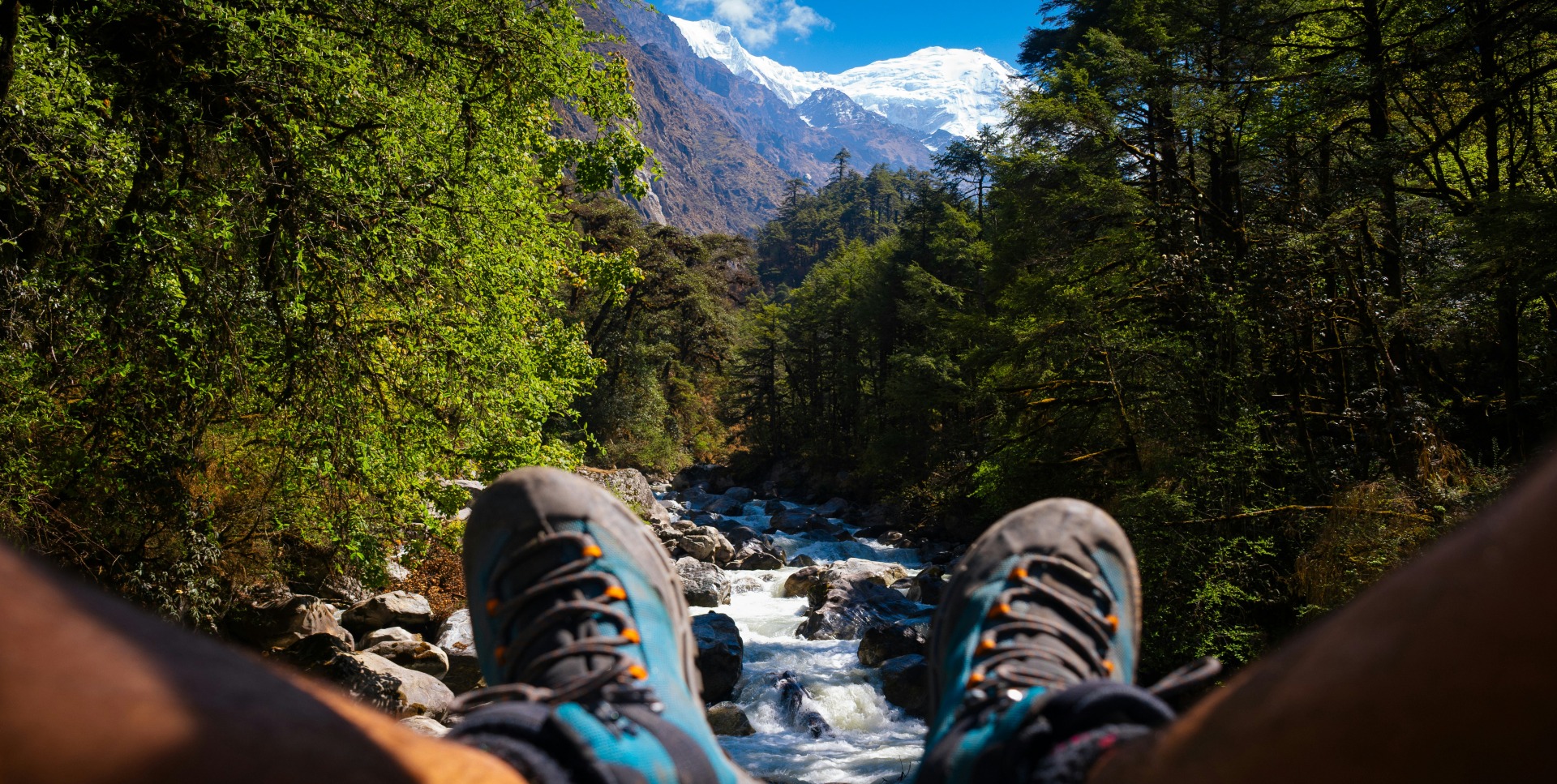 Framing the Pristine Langtang Khola River Through a Creative Perspective, Langtang Valley, Nepal A creatively framed photograph capturing the crystal-clear, glacial waters of Langtang Khola river flowing through the rugged valley, uniquely shot from between the photographer's legs, offering a distinctive and playful perspective of the Langtang landscape, Nepal.