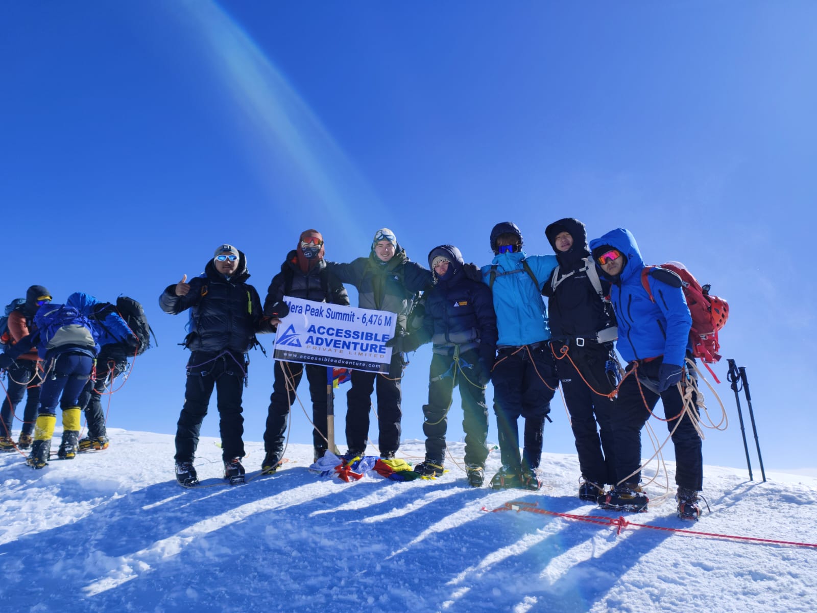 Diverse group of trekkers from Accessible Adventure Pvt. Ltd. holding an 'Accessible' banner at a mountain summit, celebrating an inclusive trekking achievement in Nepal.