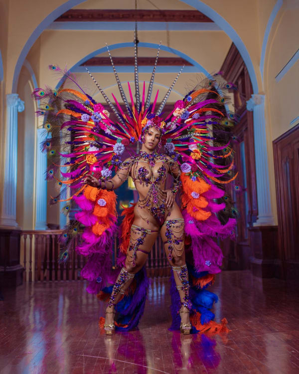 Frida from Yard Mas Carnival Jamaica Carnival 2026 wearing elaborate purple orange and pink feathered bikini costume with large backpack and headpiece
