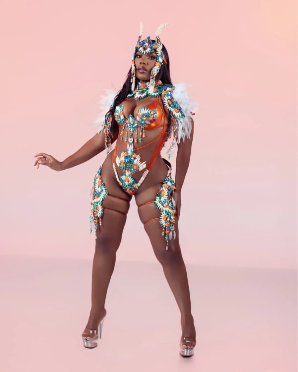 Woman in orange, teal and white beaded monokini carnival costume with feathered headpiece for One Island Band Miami Dolphins section at Miami Carnival 2026