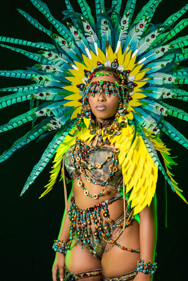Female carnival performer in yellow and teal feathered headdress and beaded bikini from Xpressionz Band Ancestral Tide – Astecz section at Saint Lucia Carnival 2026