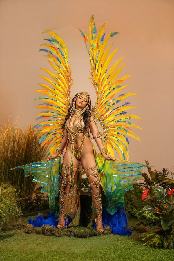 Female performer in Yuma Siren costume with large yellow blue and green feathered wings, beaded bikini and hardline pieces at Trinidad Carnival 2027