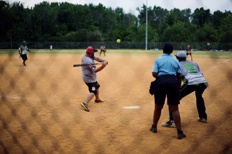 people playing softball taken through the a chain link fence behind home plate