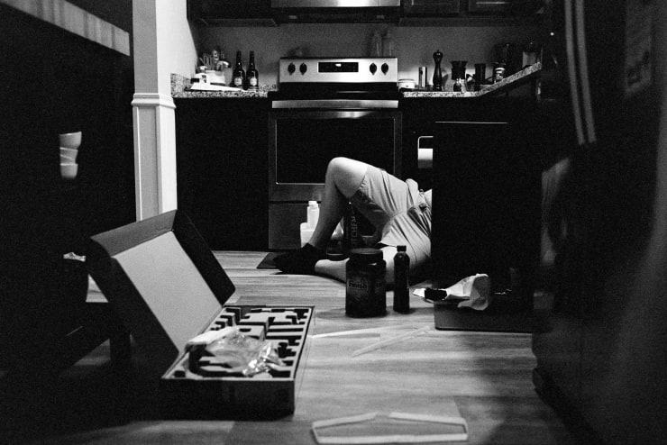 man lying on his side on a kitchen floor, half of his body is inside of the lower cabinets