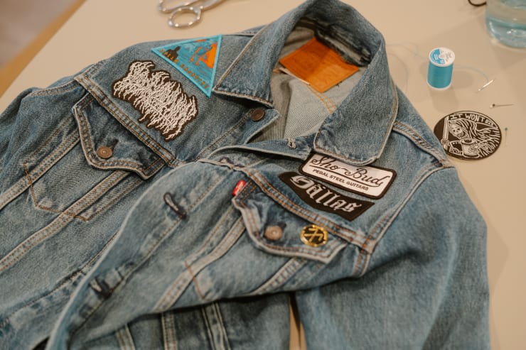 a denim jacket with various patches sewn to it sits on a table, surrounded by other sewing materials