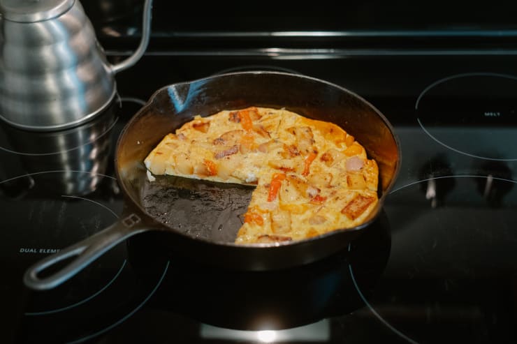 a frittata sits in a skillet on a stovetop with a slice missing