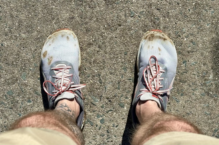 looking down at a man's legs with muddy running shoes on his feet