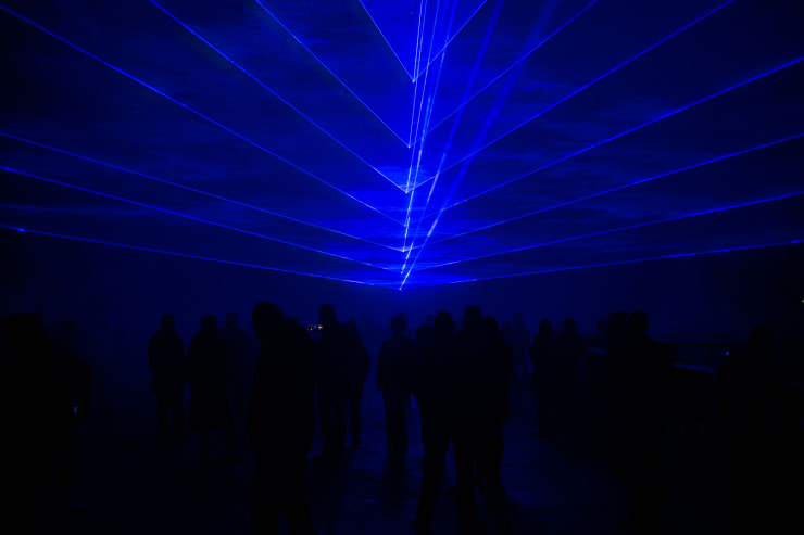 silhouette of a crowd of people under blue laser lights creating a geometic pattern