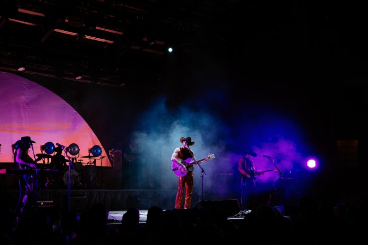 a masked country singer performs on stage with his band