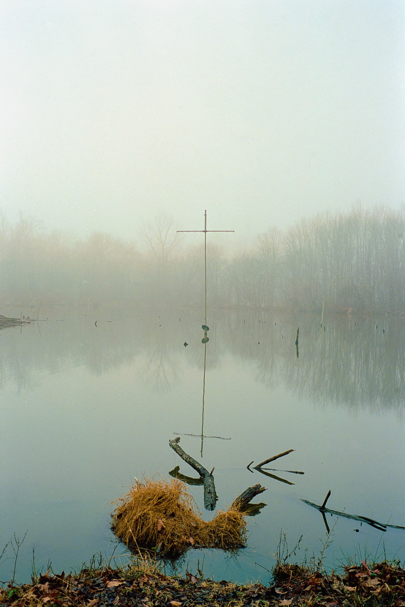 large thin cross in body of water in fog