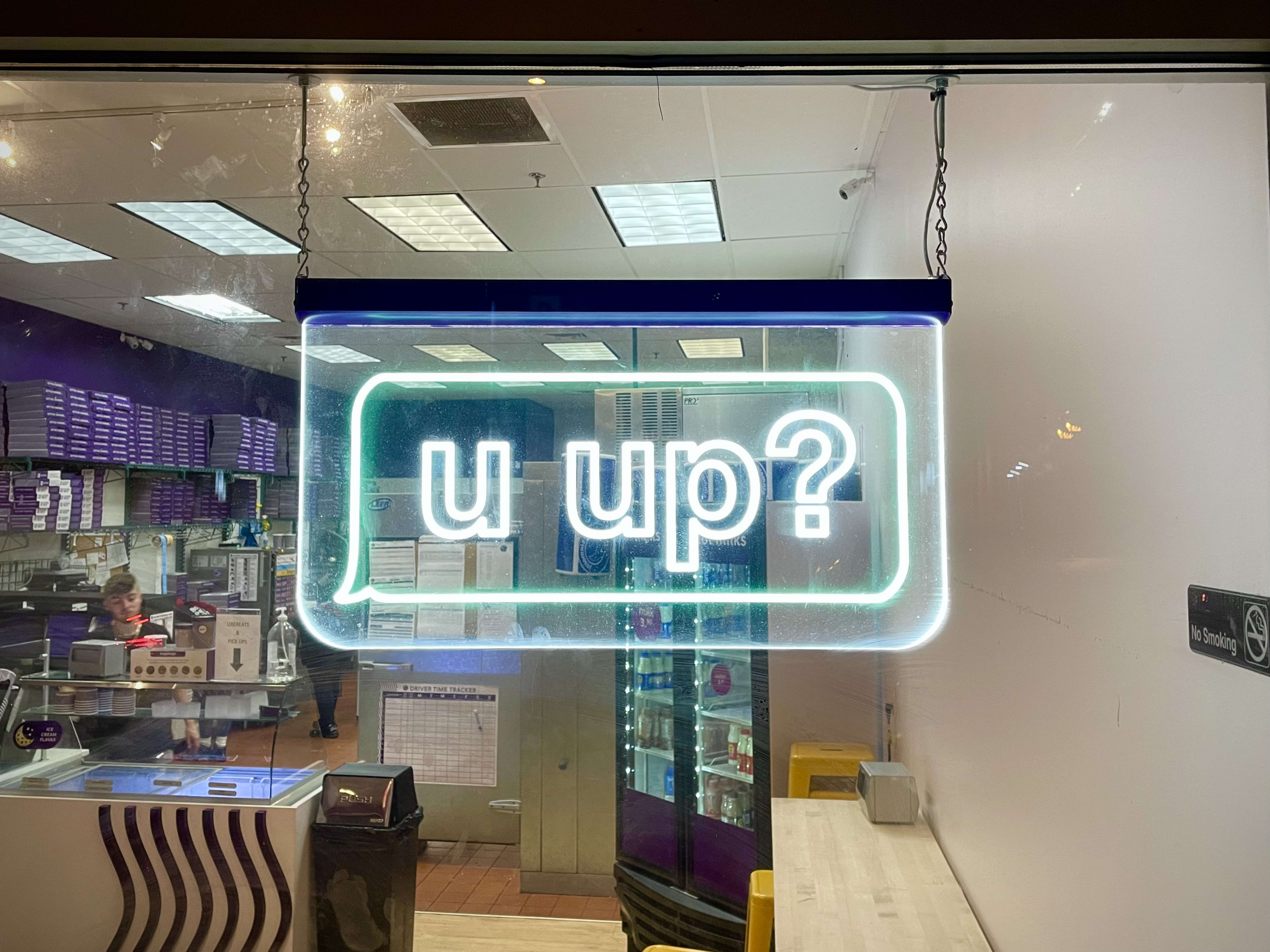 neon sign hanging in window that reads 'u up?'