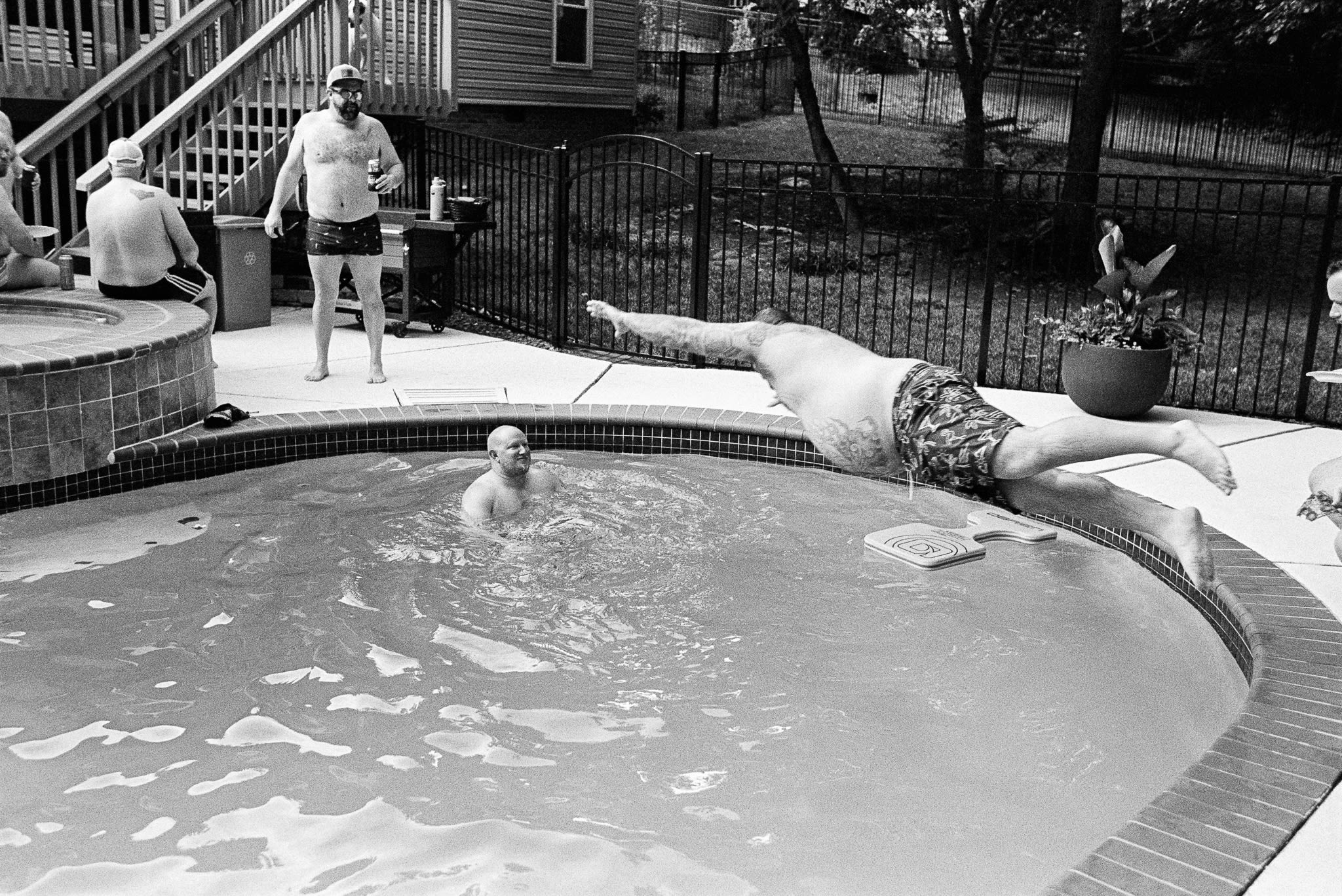 man jumping at another man in pool while others watch from the side