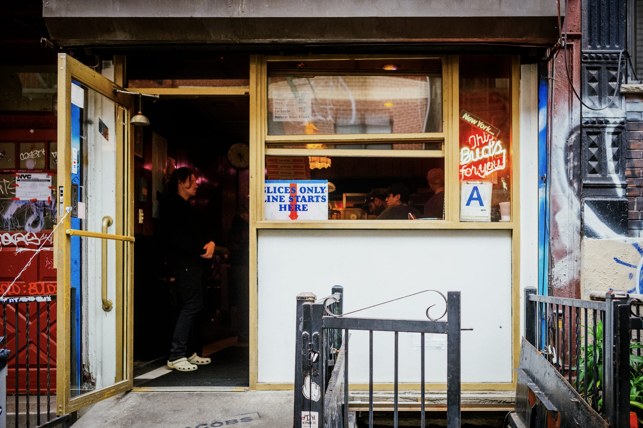 pizza joint with the door open, a sign in the window says slices only line starts here