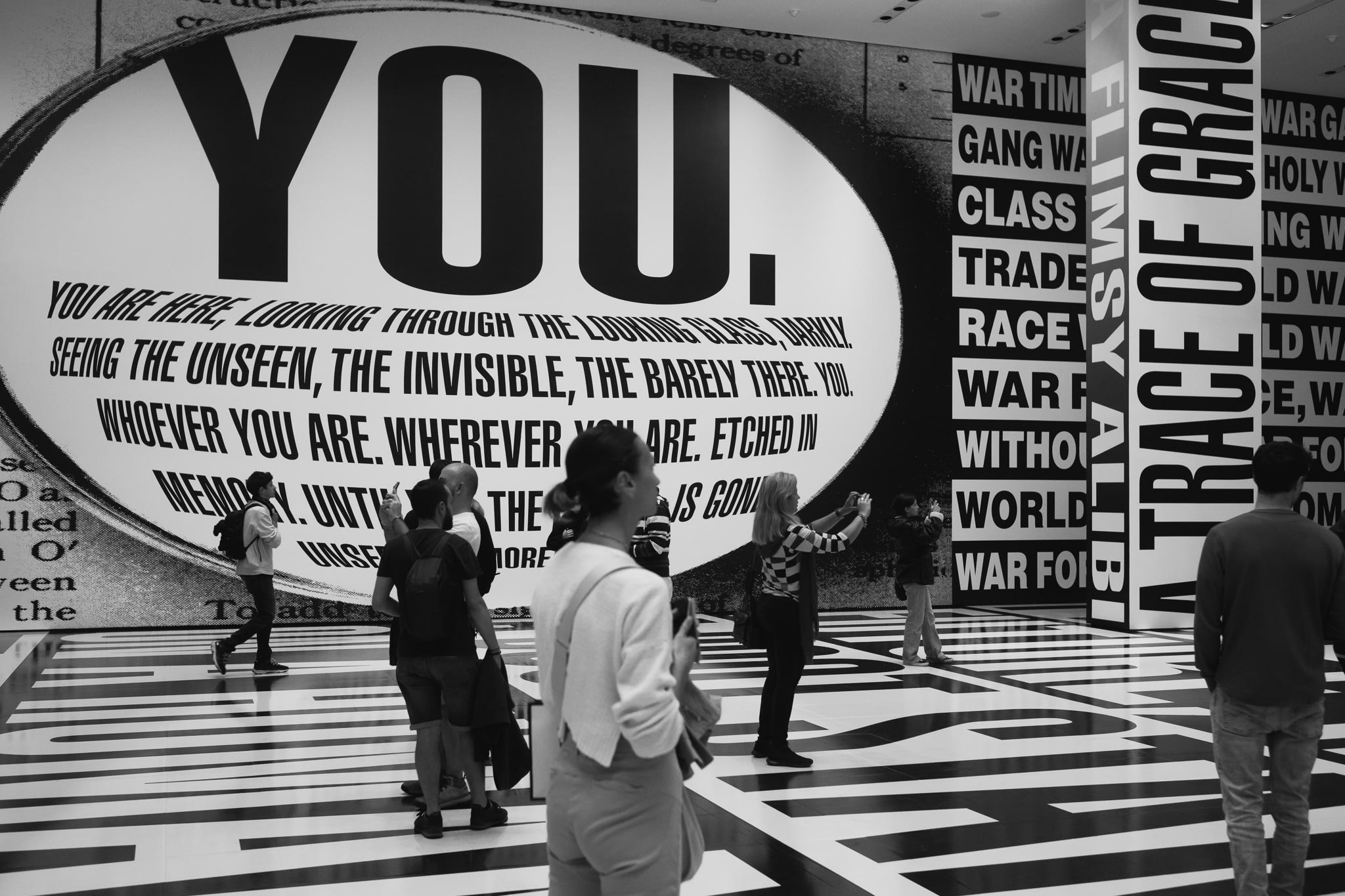 people surrounded by a large art installation made up of big bold black and white lettering covering the floor and walls