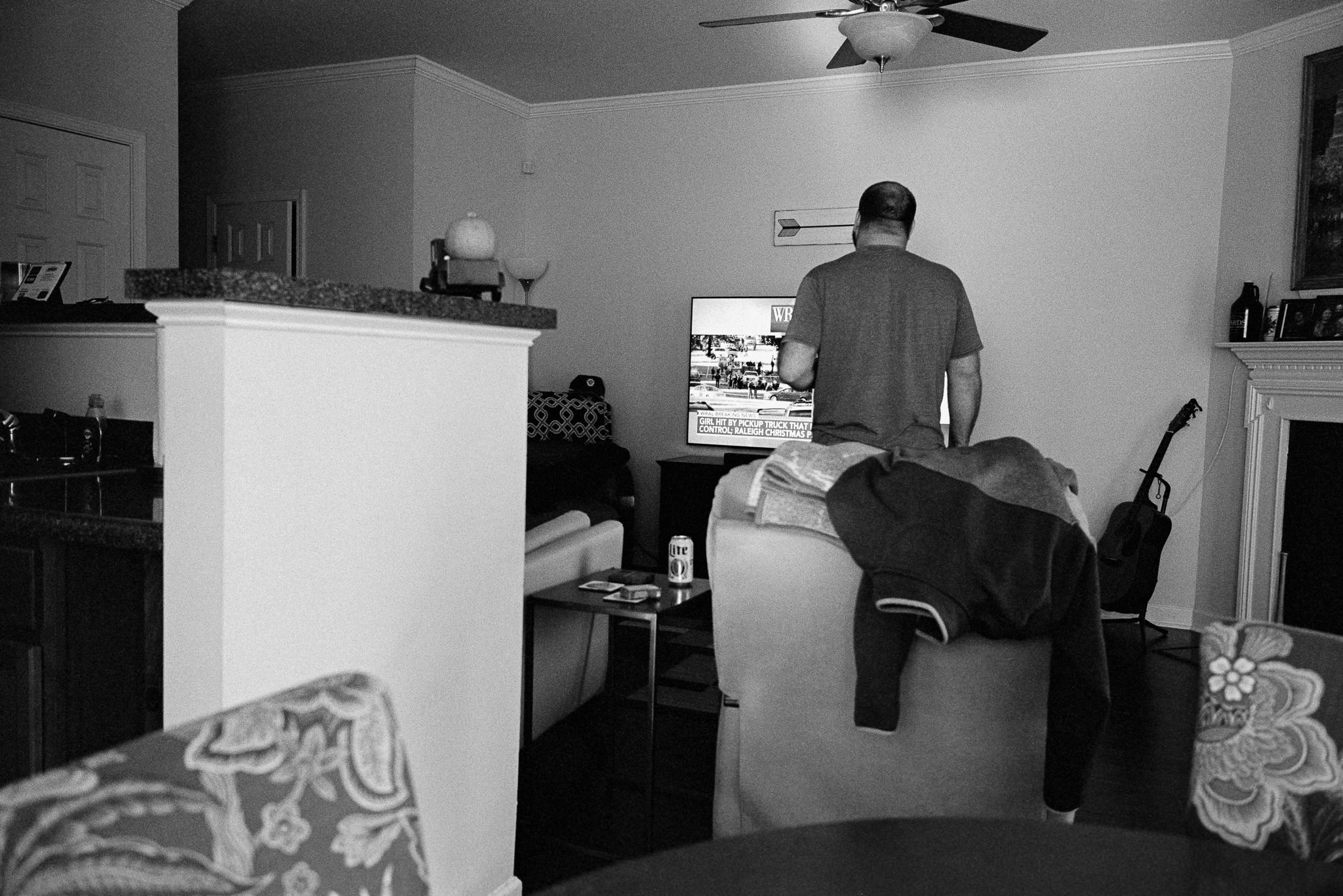 Man watching the television. The headline reads 'Girl hit by pickup truck' during the Raleigh Christmas Parade