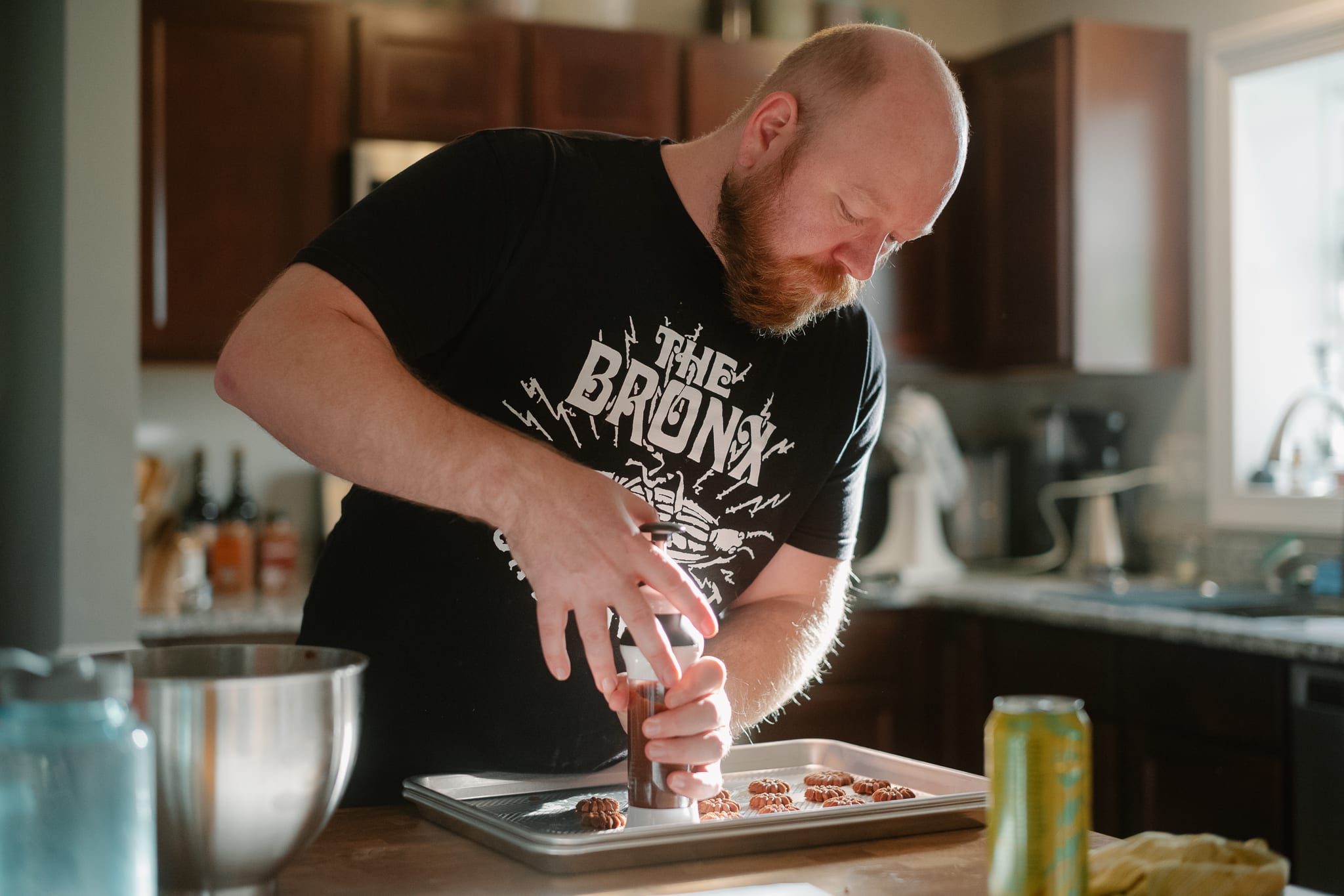 a man in a kitchen surrounded by baking equipment pressing cookies onto a sheet pan