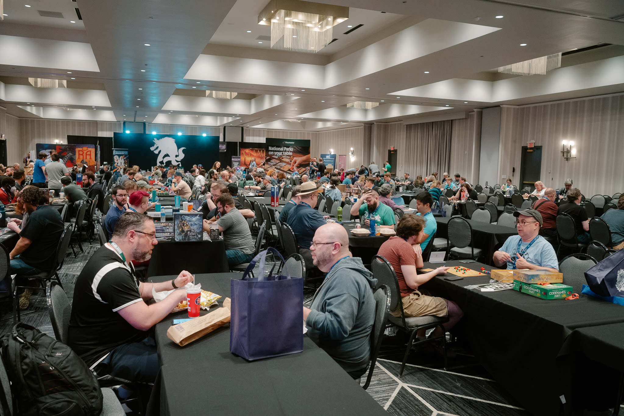 a conference room is filled with a large group of people sitting at different tables playing board games