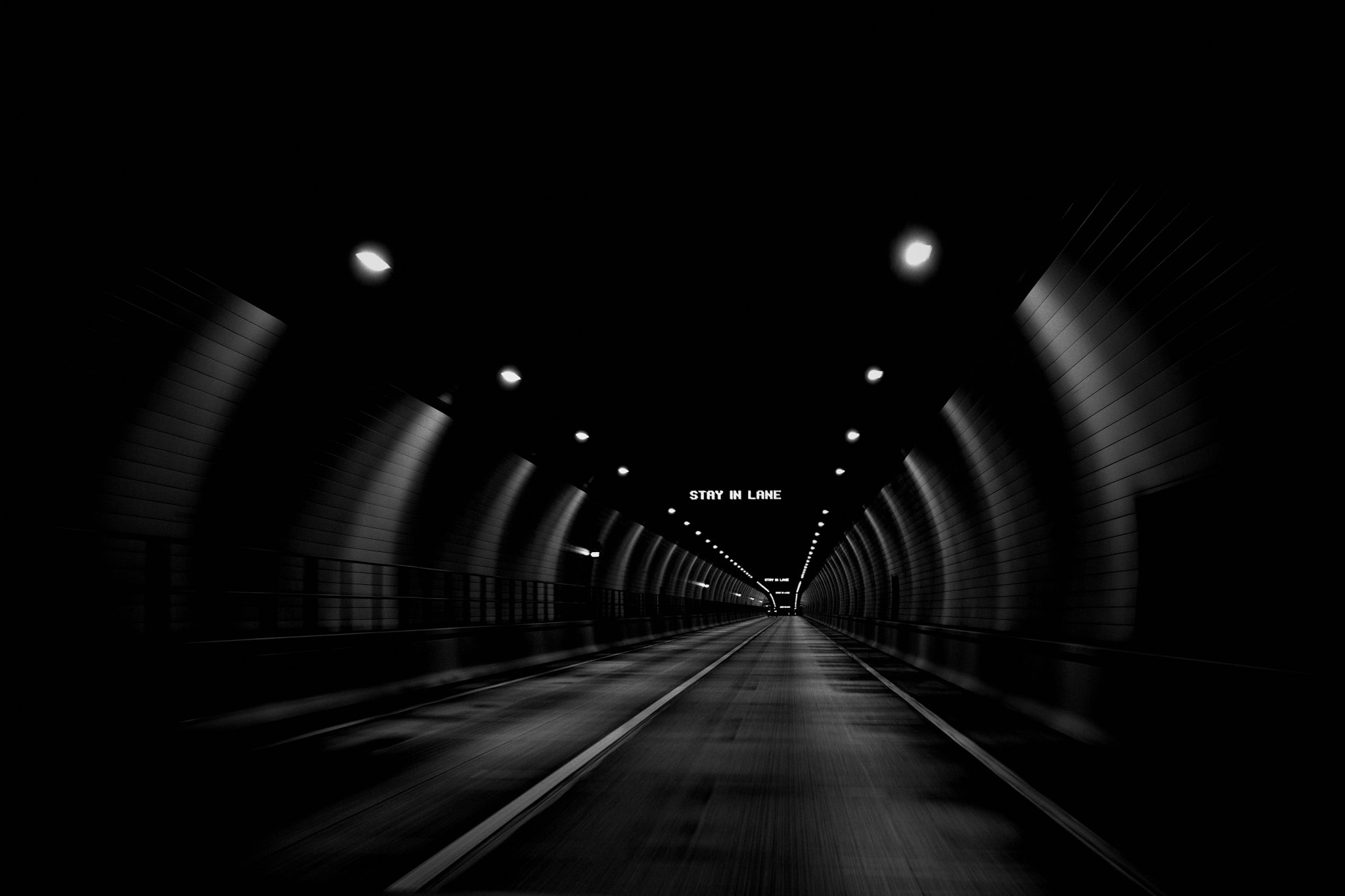 the view from a passenger seat driving through a tunnel at night. there are repeating signs that read 'stay in lane'