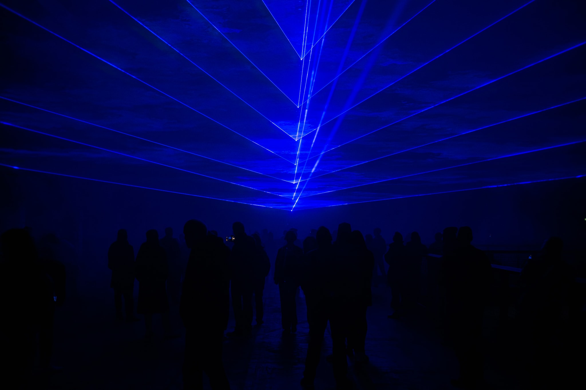 silhouette of a crowd of people under blue laser lights creating a geometic pattern