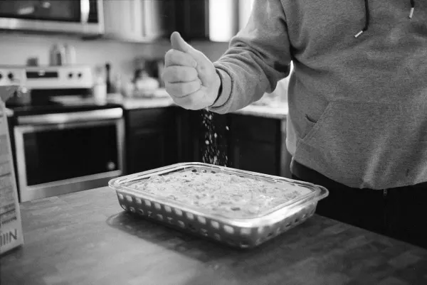 man crumbling cookies onto banana pudding dish