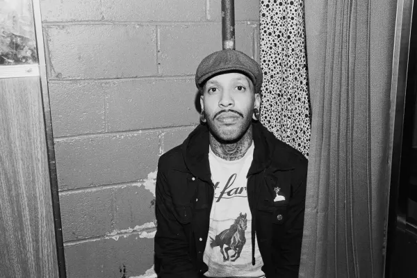 man sitting in a photo booth wearing a newsboy cap and black jacket
