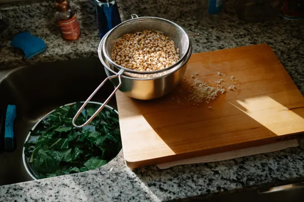 a bowl of collards washing in the sink, on the counter sits a bowl of black eye peas on a cutting board draining next to some minced garlic