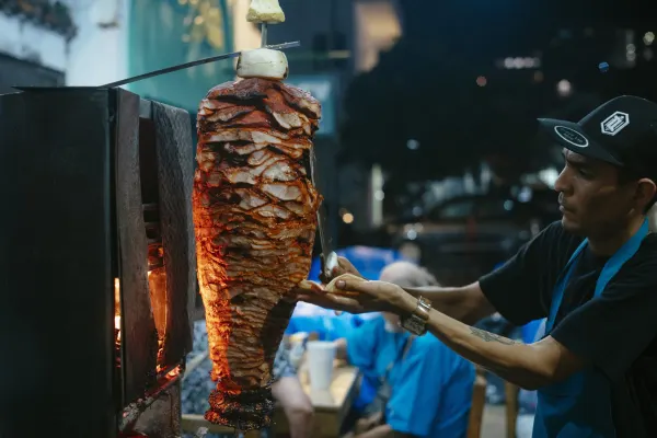 A man carves a piece of meat onto a small tortilla