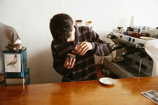 A young male barista making latte art in a small cup