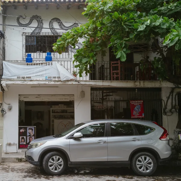 A building with a salon downstairs and a restaurant above. A small crossover SUV is parked in front.