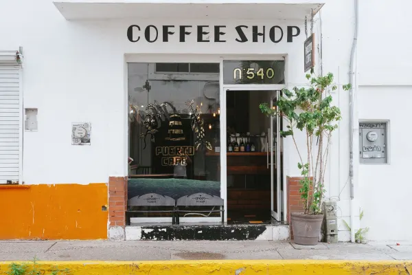 The storefront reads 'Coffee Shop' above the door. Puerto Cafe's logo is on the window. The glass door is open