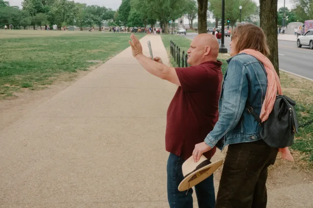 a man lining up an image of the washington monument on his smartphone while a woman observes