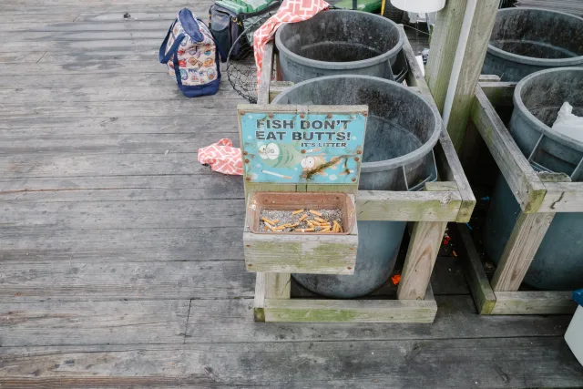 a dirty wooden ashtray built onto the pier reads 'fish don't eat butts! it's litter'