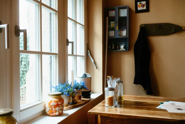 sun pours through the window of a rustic cafe, spilling onto flowers on the window sill and cutlery on a table