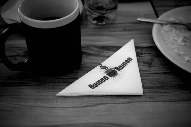 a napkin with a print that reads 'romeo und romeo' sits on a cafe table next to coffee and an empty plate