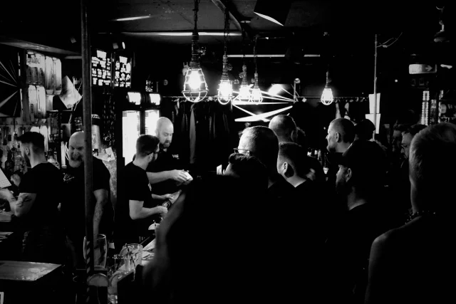 a view of a very crowded bar. people are in line to order drinks, there are four bearded men working on the other side of the bar