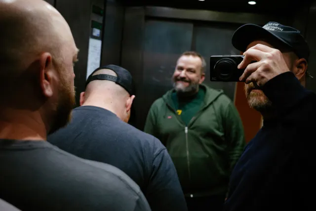 a man takes a photo of himself and three friends in a mirrored elevator