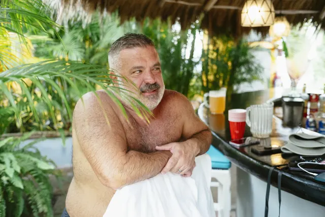 A man, still wet from the pool standing by an outdoor bar.