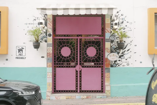 A very pretty pink metal door with a repeating circle cutout design. It is outlined by decorative tile.