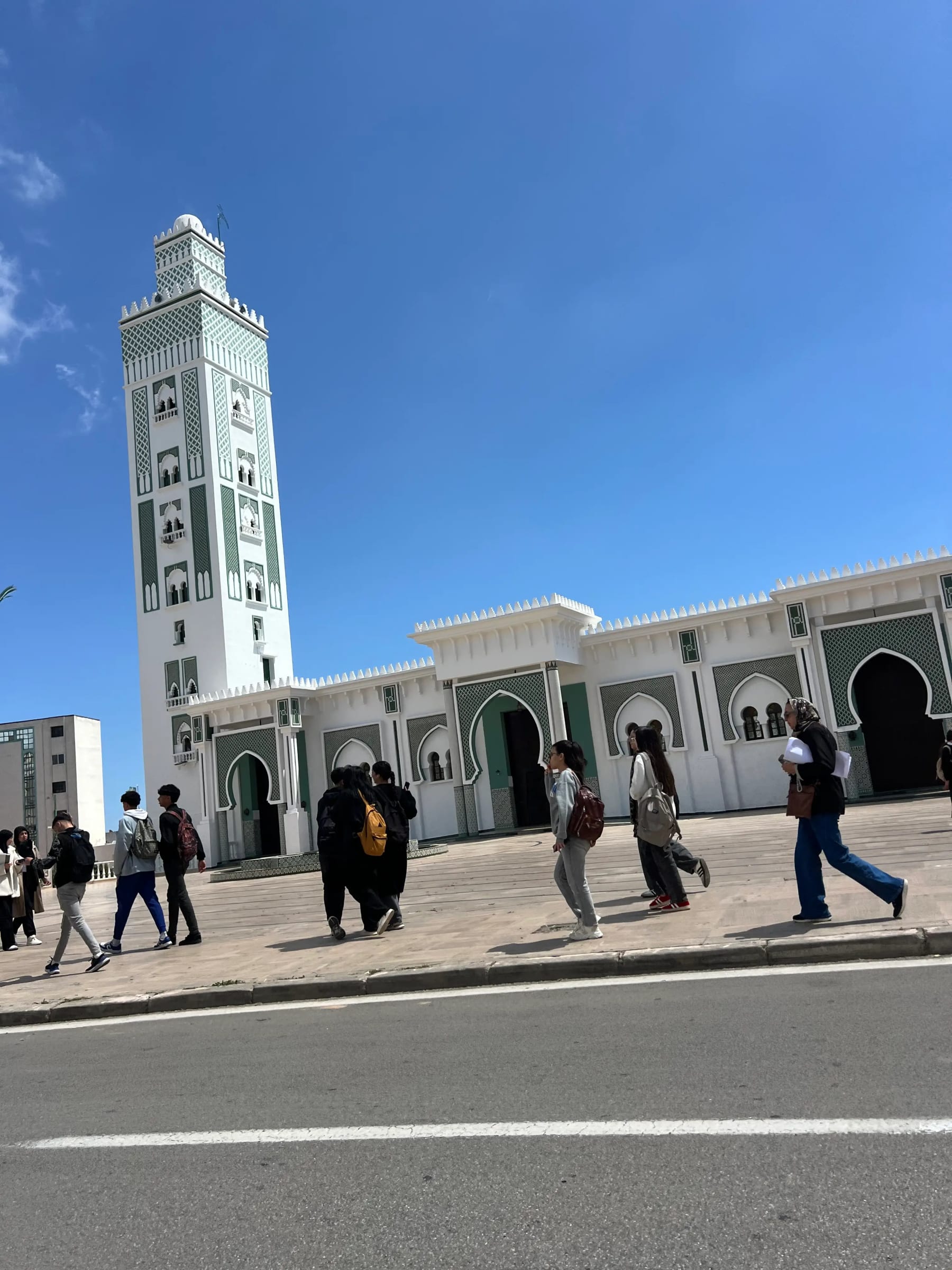 Travelers crossing the plaza beside the Grand Mosque of Tangier under a clear blue sky