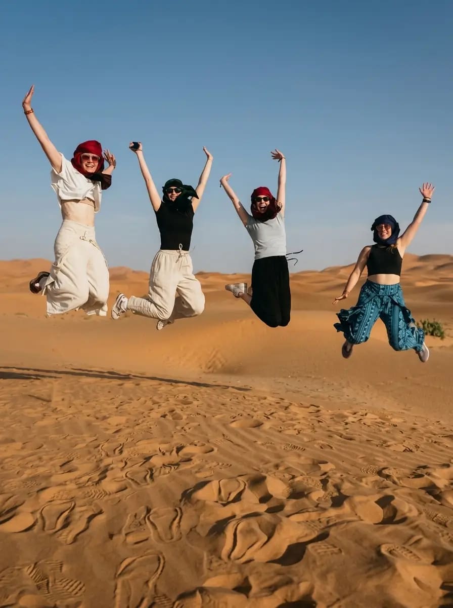 Four travelers jumping together on the golden Sahara dunes