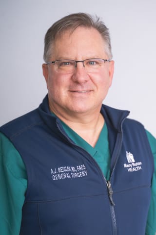 Dr. Beisler smiles at the camera in a professional photo wearing a green scrub top with a blue zipped up vest over it. 