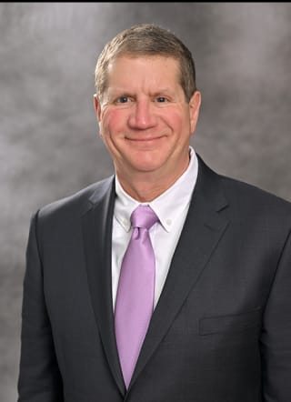 Dr. Lawrence Goldstein wearing a purple tie and black suite smiling into the camera.