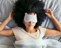 A woman lies in bed with a sleep mask over her eyes.