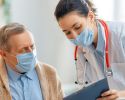A masked doctor shows her tablet to a masked patient.