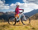 A woman stands next to her bike. There are mountains in the background.