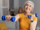 An older woman smiles as she uses a small pair of weights.