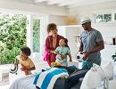 A smiling family unpacks a suitcase in a bedroom.