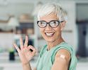An older woman with an adhesive bandage on her arm makes the OK sign.